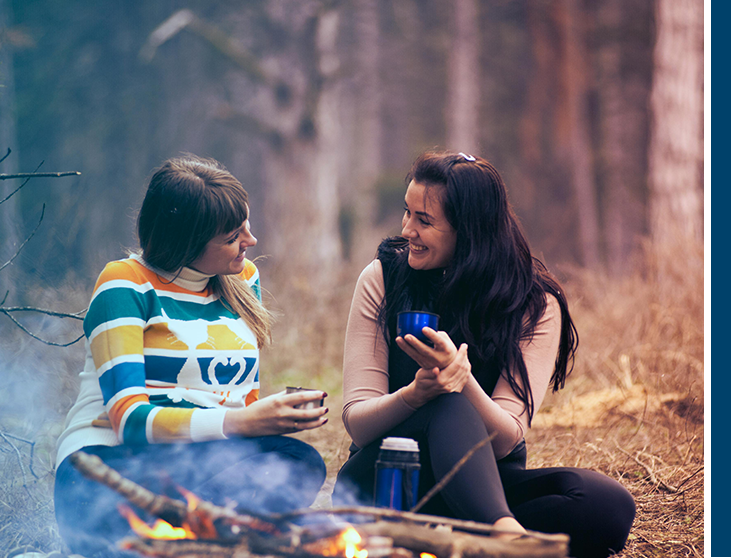 Two women sitting next to a fire in the woods.